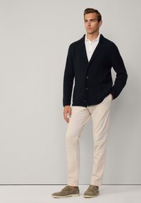 Mörkblå stickad cardigan med krage och två framfickor, tillsammans med beiga byxor och olivgröna mockaskor.