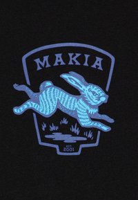 Svart t-skjorte med et blått grafikk av en hoppende kanin og teksten "MAKIA." Merkeformet med gressdetaljer og "EST. 2001" under.