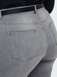 Gros plan d'une personne portant un jean en denim gris délavé et une ceinture noire, avec un accent sur la zone de la poche arrière.
