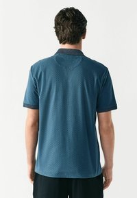 Polo de manga corta en azul oscuro con una tela texturizada, presenta un cuello en contraste y un corte ligeramente holgado.