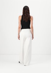 Zwarte geribbelde mouwloze top gecombineerd met witte wijde broek. De broek heeft een gladde textuur en een elastische tailleband.