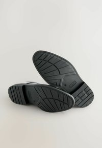 Chaussures à semelle en caoutchouc noir avec un motif de structure en relief, dotées d'une partie supérieure lisse avec des détails contrastés et un design à bout arrondi.