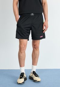 Melnas acs sporta bikses ar elastīgu jostasvietu, ar rozā adidas zīmolu un zaļiem un ziliem akcentiem malās.