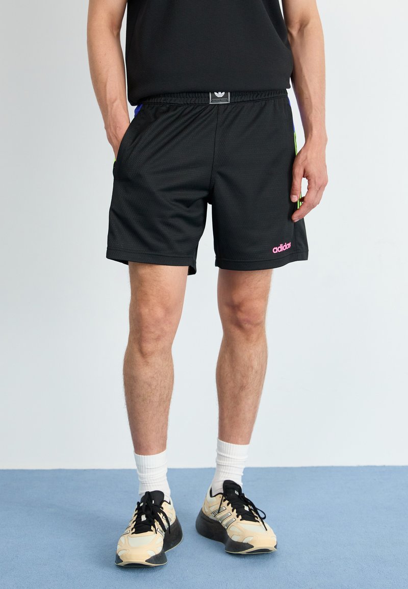Melnas acs sporta bikses ar elastīgu jostasvietu, ar rozā adidas zīmolu un zaļiem un ziliem akcentiem malās.