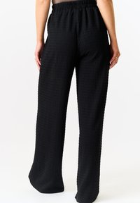 Black wide-leg pants made of textured fabric, featuring an elastic waistband and a relaxed fit, with a smooth surface and subtle pattern.
