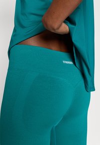 Τύρκουαζ αθλητικό κολάν με λείο υφή, διαθέτοντας φαρδύτερη μέση με την ένδειξη "STRONGER" και εφαρμοστή σχεδίαση που αναδεικνύει το σχήμα.