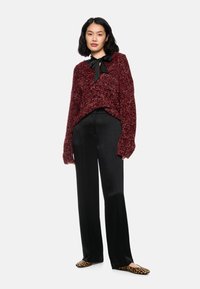 Burgundy knitted sweater with a loose fit and textured surface; paired with black wide-leg pants and leopard-print flats. Black ribbon accent.