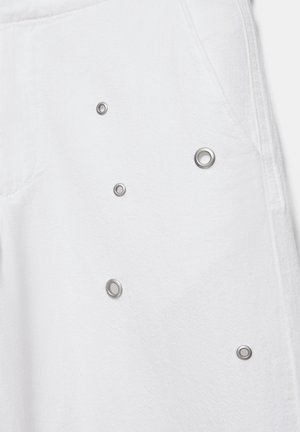 Hvidt stof med fem sølvfarvede metal-øjer i forskellige størrelser tilfældigt arrangeret nær en søm og lommeomrids.