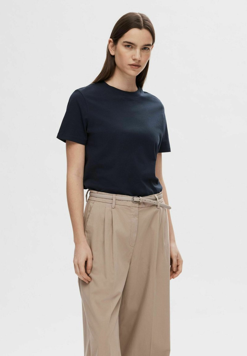 Marineblauwe katoenen t-shirt met korte mouwen, gecombineerd met lichtbeige hoog-snit broek met een riem en geplooid voorkantdetail.