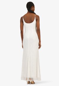 Weißes Abendkleid mit Perlen, figurbetontem Schnitt, Spaghettiträgern und einem dekorativen fransigen Saum, der wellenartige Perlenmuster präsentiert.