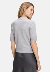 Jasnoszara, krótko rękawowa bluzka z dopasowanym krojem i prążkowanymi krawędziami. Miękka tekstura, minimalistyczny styl i wysoki dekolt.