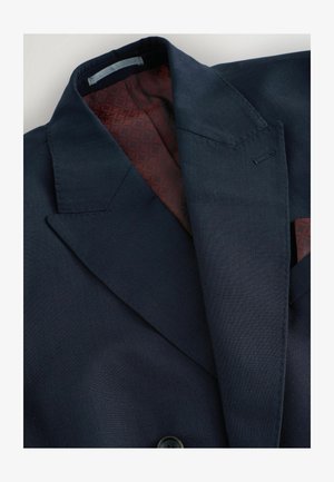 Blazer blu navy con revers appuntiti e doppio bottone. L'interno presenta una fodera bordeaux testurizzata con motivo geometrico.