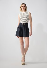 Haut sans manches rayé blanc associé à un short taille haute bleu marine foncé avec une boucle circulaire marron et deux poches avant.