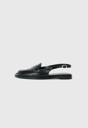 Zapato slingback de cuero negro con punta redonda, suela plana, corte lateral y correa que presenta un detalle de hardware en tono dorado.