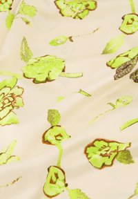 Gepubliceerd stof met een crèmekleurige achtergrond en levendige groene bloemontwerpen, aangevuld met bruine omkeringen en een gladde textuur.