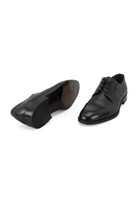 Zwarte leren schoenen met een spitse neus, gestructureerde bovenkant en een gladde neuskap. Heeft veters en een lage, rechthoekige hak.