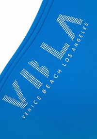 Blauer Stoff mit einer glatten Textur zeigt ein bedrucktes Design mit den Wörtern "VIBLA" und "VENICE BEACH LOS ANGELES" in weißen, gepunkteten Buchstaben.