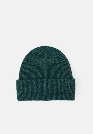 Bonnet tricoté en côtes vert foncé avec revers plié, posé à plat sur un fond clair uni.