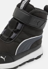 Černá a šedá sportovní bota s polstrovaným límečkem, popruhem na suchý zip, texturovanou látkou a gumovou podrážkou s výrazným vzorem.