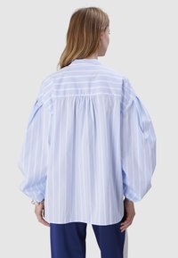 Light blue striped blouse with puffed sleeves, a gathered back, and a collared neckline, made from soft cotton fabric.