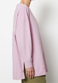 Sudadera rosa claro de gran tamaño con cuello redondo, hombros caídos, aberturas laterales y puños acanalados, fabricada con una tela suave y texturada.