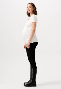 Maternity kortærmet top i hvid, kombineret med sorte leggings og høje sorte støvler. Glat tekstur med en tætsiddende design, der fremhæver maven.