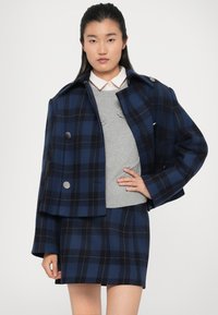 Navy og blåternet uldblandingsjakke med oversized klapper og dobbeltknapper, parret med en grå sweater og en matchende nederdel.