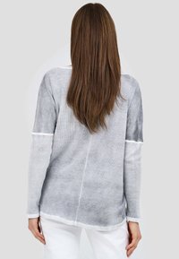 Grå långärmad topp med en strukturerad mönster, vita detaljer, en avslappnad passform och en rundad avslutning, som visar ett lätt tyg.