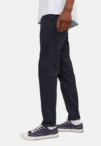 Chinos bleu marine en coton, à coupe droite et avec des manches retroussées, associés à des baskets sombres avec des accents blancs et des lacets.