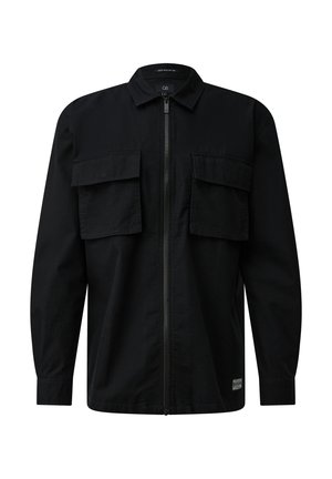 Veste-chemise noire à manches longues avec fermeture éclair frontale et deux grandes poches à rabat sur la poitrine, petite étiquette près de l'ourlet inférieur.
