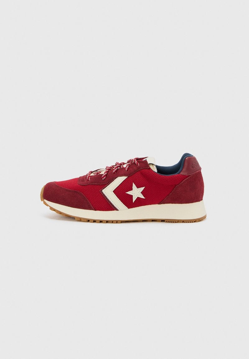 Baskets basses rouges avec logo étoile blanche et chevron, semelle blanche, semelle extérieure en gomme et lacets à motifs sur un fond clair uni.