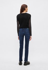 Suéter negro con mangas transparentes, jeans azul oscuro de corte ajustado y zapatos negros con plataforma. Vista desde atrás, mostrando la textura del denim y detalles de costura.