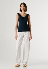 Marinblå ärmlös topp med rynkad V-ringning, kombinerad med vita vida byxor och beige sneakers med vita detaljer. Mjukt material och figurnära passform.