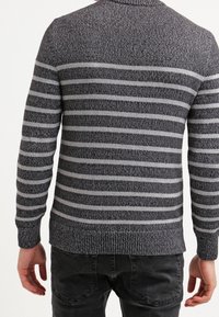 Maglione a righe grigie e nere in maglia con colletto rotondo, polsini e orlo a costine. Il tessuto testurizzato mostra una combinazione di righe chiare e scure.