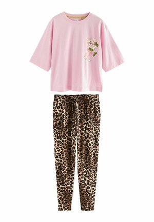 Kvinde i pink skjorte og leopardbukser sidder barfodet på en mønstret stol, holder en jordbær over det ene øje nær en julekrans og et bord med drikkevarer.