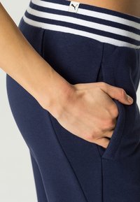 Navy jogger pants with white striped elastic waistband; features side pocket; made of soft, stretchy fabric with a smooth texture.