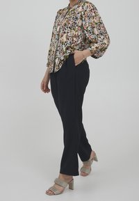 Blusa floreale con maniche a sbuffo, base nera con fiori multicolori. Abbinata a pantaloni larghi blu scuro e sandali con tacco beige.