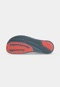 Semelle de chaussure avec une bande de roulement en caoutchouc gris et rouge composée de rainures et de motifs texturés pour la traction.