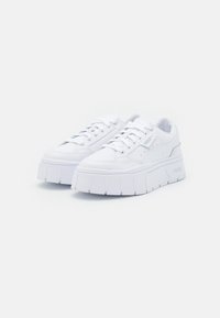 White platform sneakers with a smooth leather upper, reinforced toe cap, thick rubber sole, and subtle branding on the side.