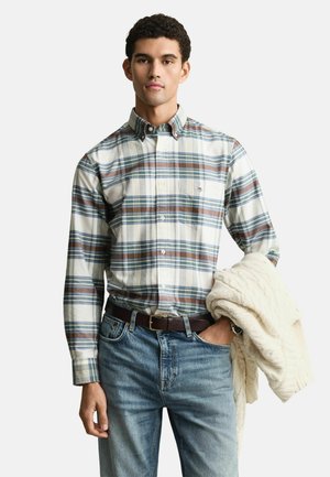 Karierter Button-down-Hemd in Weiß-, Blau- und Brauntönen; aus Baumwolle. Getragen mit blauen Jeans und hält einen cremefarbenen Strickpullover.