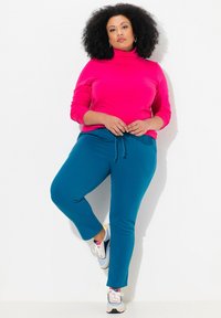 Rosa polotröja kombinerad med teal joggingbyxor. Joggingbyxorna har en dragsko vid midjan, medan sneakers har grå och vita detaljer.