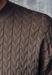Brązowy sweter z fakturowanym splotem przypominającym serca, z prążkowanym kołnierzem i miękkim materiałem, podkreślający ciepło i komfort.