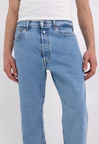 Jeans in denim blu chiaro con taglio dritto, cinque tasche e chiusura a bottone metallico. Presentano un leggero sbiadimento e dettagli di cucitura arancioni.