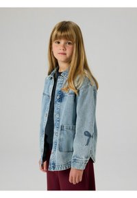 Gaiši zilas džinsa jaciņas ar pogu priekšpusi, divām priekšējām kabatām un lokas dizaina detaļu uz kreisās piedurknes. Brīva pieguluma.