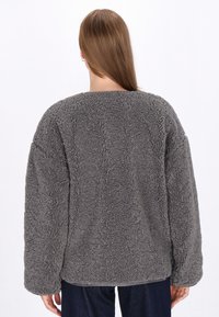 Grauer Fleece-Pullover mit einer weichen, strukturierten Oberfläche, weiten Ärmeln und einem abgerundeten Ausschnitt. Die Rückansicht zeigt ein einfaches, klares Design.