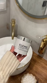 Barattolo circolare bianco con coperchio argento etichettato "ELEMIS Dynamic Resurfacing Facial Pads." Design texturizzato e superficie liscia. Maglione beige a maglia visibile.