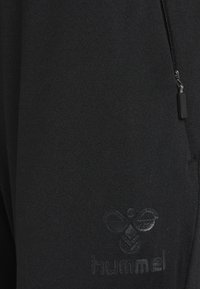 Svarta träningsbyxor med en slät yta, diskret präglad logotyp och en ficka med dragkedja för förvaring.