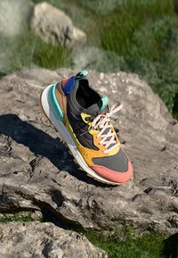 Sneaker featuring a black mesh upper, orange and yellow accents, pink laces, and colorful sections of leather on the heel and tongue.