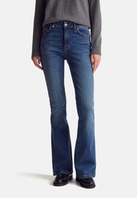 Jeans de mezclilla azul de campana con una cintura alta, que cuentan con bolsillos frontales, costuras visibles y una parte superior ajustada. La tela tiene una textura suave.