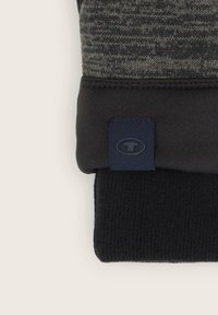 Knitted glove cuff in shades of gray and black, featuring a smooth texture and a small blue logo patch on the side.
